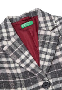 Cappotto in misto lana a quadri grigio e bianco con dettagli rosa; presenta un colletto a punta, un solo bottone nero e fodera bordeaux. Etichetta visibile.