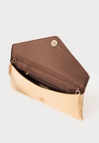 Kuvitus beigen värisestä tekonahkasta valmistetusta clutch-laukkusta, jossa on tekstuuri pinta, kultasävyiset yksityiskohdat, magneettisulku sekä ruskealla kankaalla vuorattu sisustus, jossa on vetoketjullinen tasku.