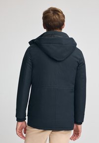 Giacca blu navy scuro con cappuccio, caratterizzata da una texture liscia e un taglio dritto, cuciture visibili e dettagli a coste sui polsini.