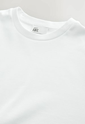 Weißes Baumwoll-T-Shirt mit geripptem Rundhalsausschnitt und normalem Schnitt. Das Etikett trägt die Aufschrift "NEXT EDIT." Der Stoff wirkt glatt und unstrukturiert.
