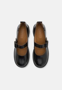 Czarne skórzane buty typu Mary Jane z okrągłym noskiem, regulowanym paskiem na klamrę oraz brązową wkładką; gładka faktura i minimalistyczny design.
