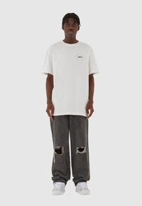 Hvit kortermet t-skjorte med en liten turkise logo, paret med mørkegrå ripped jeans og hvite joggesko. Enkel, avslappet passform.