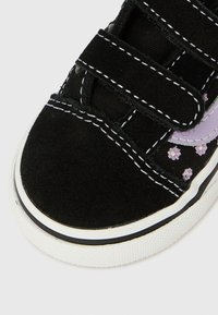 Sneaker in suede nero con cinturini in Velcro, cuciture bianche, tela nera strutturata, dettagli floreali viola e suola in gomma bianca.
