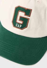 Kottongenser med grønn skjerm og kremhvit kropp. Har en brodert grønn og brun "GAP"-logo i en oktagonal design.