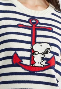 Maglione a righe con linee orizzontali blu navy e bianche, caratterizzato da un'ancora ricamata rossa e un personaggio dei cartoni animati al centro.