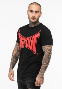 Sort bomulds T-shirt med et stort rødt "TAPOUT" logo hen over brystet, rund hals og korte ærmer. Mønstret varierer på stoffets tekstur.
