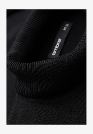 Zwarte trui met een hoge, geribbelde kraag. Het materiaal lijkt textuur te hebben, met een gladde body. Het binnenlabel toont de merknaam en maat.