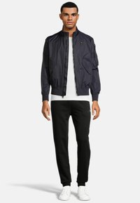 Navy bomberjack met een ritssluiting aan de voorkant, geribbelde manchetten en twee zijzakken. Gecombineerd met zwarte sweatpants en witte sneakers.