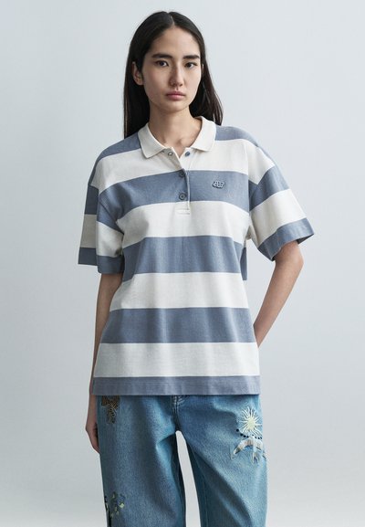 Polo rayé en mélange de coton doux, présentant des rayures horizontales bleues et crème, un col et trois boutons. Design décontracté et confortable.