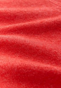 Tissu rouge texturé avec une apparence douce et tricotée, présentant des variations subtiles de teinte et d'épaisseur à travers le matériau.