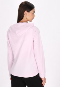 Jasnoróżowa bluza z kapturem, z długimi rękawami. Miękka tkanina, zaokrąglony dół i prosty design. Brak widocznych wzorów lub detalów sprzętowych.