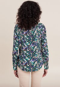 Langarmhemd mit einem bunten Blumenmuster in Grün, Blau und Lila auf einem cremefarbenen Hintergrund; abgerundeter Saum und Knopfmanschetten.