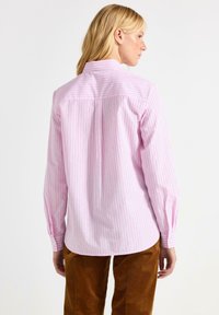 Lyserød stribet langærmet skjorte med knapkrave. Har lodrette striber i forskellige bredder og manchetter på ærmerne.