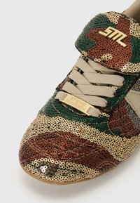 Pailletten sneakers in camouflagepatroon met groene, bruine en beige kleuren. Inclusief een gouden logo en beige veters. Textuur oppervlak.
