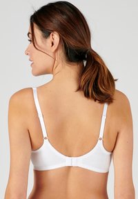 Sostenitore bianco con spalline regolabili, una texture di tessuto liscia e una chiusura a gancio e occhiello sul retro. Due piccoli dettagli circolari sulle spalline.