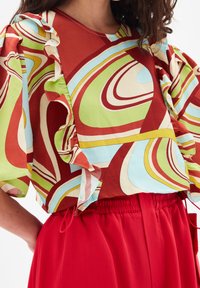 Top multicolore con un motivo ondulato in rosso, verde e blu. Presenta maniche arricciate e un collo rotondo, abbinato a una gonna rossa con vita elastica.