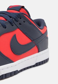 Sneaker Nike con una parte superiore in pelle blu navy e rossa brillante, con accenti testurizzati e una suola in gomma bianca. Presenta lacci e dettagli cuciti.