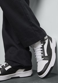 Zwart-witte sneakers met leren en textiele materialen. Kenmerken zijn onder andere een geperforeerde neus, contrasterende strepen en een opvallend logo op de hiel.