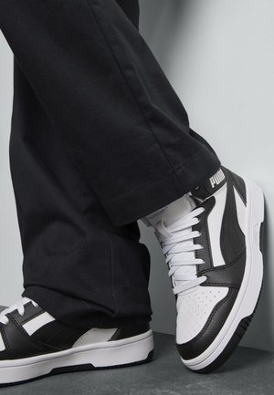 Zwart-witte sneakers met leren en textiele materialen. Kenmerken zijn onder andere een geperforeerde neus, contrasterende strepen en een opvallend logo op de hiel.