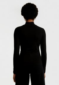 Zwarte coltrui met lange mouwen, aansluitend ontwerp, zachte textuur, hoge hals en subtiele stikdetails. Effen kleur zonder patronen.