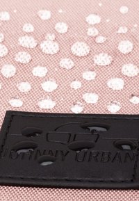 Ljusrosa tyg med upphöjda vita prickmönster, med en svart texturerad logotagg som visar "Johnny Urban" längst ner.