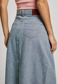 Lichtblauwe denim rok met een hoge taille, twee achterzakken en een bruine leren patch op de tailleband. Gladde textuur met een lichte glans.