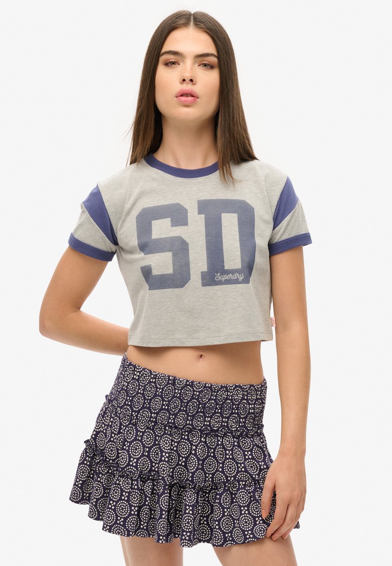 Afgekorte grijze t-shirt met marineblauwe mouwen en "SD" druk, gecombineerd met een marineblauwe rok met witte circulaire patronen en een gerimpelde zoom.