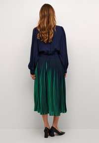 Bluză bleumarin cu fustă plisată av�ând dungi verticale de la verde închis la verde deschis, purtată cu pantofi cu toc negri.