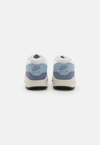 Nike Air tenisice s gornjim dijelom u svijetloplavoj i sivoj boji, bijelim akcentima, glatkom teksturom i crnom gumom potplatom. Logotip prikazan na peti.