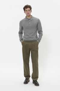 Polo a maniche lunghe grigio con colletto e patta dei bottoni, abbinato a pantaloni verde oliva a pieghe e scarpe stringate marroni.