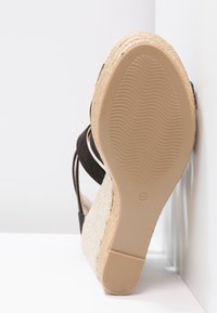 Sandale espadrille compensée avec talon en jute tressée, semelle en caoutchouc beige taille 37 et brides de cheville noires sur fond blanc.