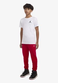 Balta kokvilnas T-kreklā ar melnu Jordan logotipu, apvienots ar sarkaniem sporta biksēm ar baltu logotipu un melniem augstiem sporta apaviem ar sarkaniem akcentiem.