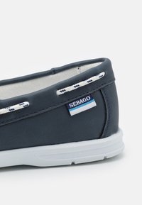 Navyfarbene Slipper mit Obermaterial aus glattem Leder, weißer Gummisohle und dekorativen weißen Schnürsenkeln. Mit einem blauen und weißen Logoetikett.