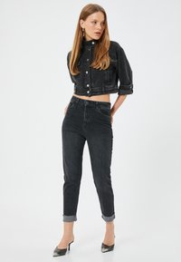 Chaqueta corta de mezclilla negra con botones plateados, y jeans de cintura alta a juego. Ambos presentan un diseño clásico de cinco bolsillos y mangas enrolladas.