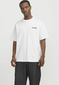 Hvid bomulds t-shirt med korte ærmer og rund hals, prydet med sort tekst "CNZ-MOV" nær venstre bryst, afslappet pasform.