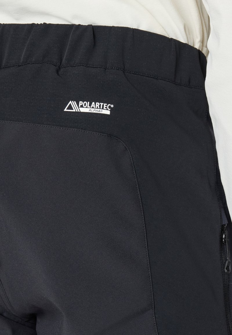 Schwarze Polartec Alpha Isolationshose mit elastischem Bund und sichtbarer Reißverschlusstasche an der Seite.