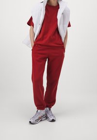 Rotes Baumwoll-T-Shirt und passende Jogginghosen, kombiniert mit einer weißen gepolsterten Weste. Strukturierte Sneakers mit silbernen und roten Akzenten.