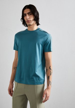 Teal kortærmet t-shirt i blødt stof, med rund halsudskæring og kontrasterende lyseblå detaljer langs skuldrene.