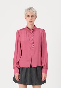 Pink long-sleeve blouse with ruffled collar, button front, and decorative shoulder accents. Soft fabric with a smooth texture.