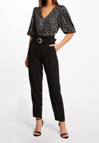 Svart mönstrad blus med V-ringning, tillsammans med hög midja svarta byxor med ett dekorativt bälte och eleganta svarta sandaler.