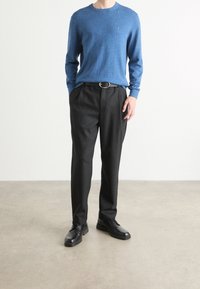 Niebieski melanżowy sweter dziergany w zestawie z czarnymi spodniami. Spodnie mają luźny krój. Czarny obuwie dopełnia strój.