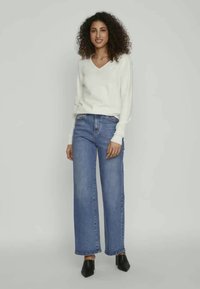 White v-neck sweater paired with high-waisted, wide-leg blue jeans. Black pointed-toe shoes. Smooth textures and casual design.