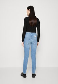 Gaiši zili, šauri džinsi ar nodilušu tekstūru, ar augstu jostasvietu un aizmugures kabatām. Apvienoti ar pieguļošu melnu krekla ar garām piedurknēm.