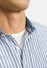Camicia a righe blu e bianca con colletto a contrasto navy. Il tessuto è leggero con una texture visibile e dettagli fini.