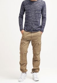 Camicia a maniche lunghe blu navy con un motivo testurizzato, abbinata a pantaloni cargo beige con più tasche e stirate sulle caviglie. Sneakers bianche.