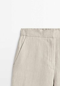 Pantalon beige clair avec une texture en chevrons, doté d'une ceinture plate et de poches latérales. Le tissu semble doux et léger.