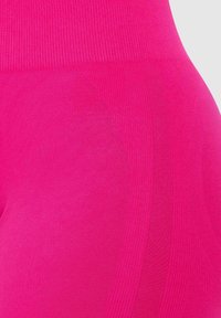 Dopasowane legginsy o wysokim stanie w intensywnym różowym kolorze. Wykonane z teksturowanej tkaniny z prążkowanym pasem i gładkimi obszarami po bokach.