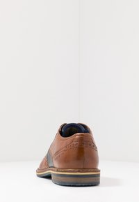 Chaussure en cuir marron avec des perforations, panneaux en tissu gris, bout rond et semelle cousue. Vue arrière montrant le col rembourré et l'accent sur le talon.