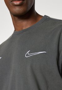 Dark gray crewneck sweatshirt with white Nike swoosh logos on the front. Features soft fabric and casual fit.