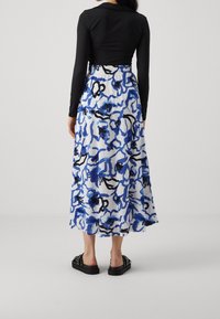 Černý top s dlouhým rukávem a přiléhavým střihem doplněný vzdušnou sukní s délkou po kolena, která má bílý základ s modrými abstraktními vzory. Černé boty.